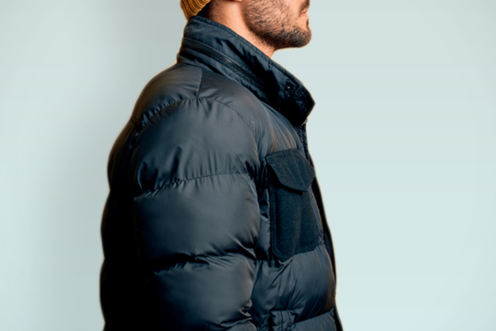 A snowboarder stands atop a snowy mountain holding his snowboard with the back facing the camera. The snowboard artwork reads Hydrogen, in a script font.
