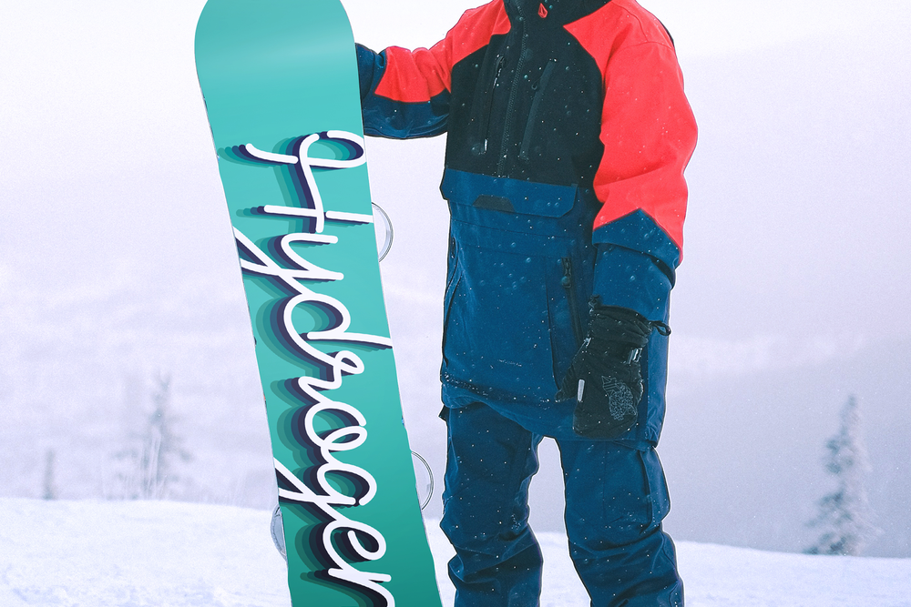 A snowboarder stands atop a snowy mountain holding his snowboard with the back facing the camera. The snowboard artwork reads Hydrogen, in a script font.